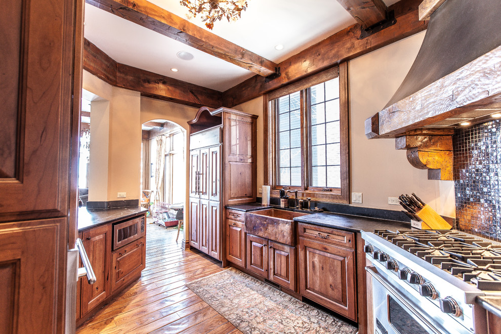 Photo of a large traditional galley kitchen in Other with a farmhouse sink, raised-panel cabinets, medium wood cabinets, soapstone benchtops, mosaic tile splashback, stainless steel appliances, medium hardwood floors and no island.
