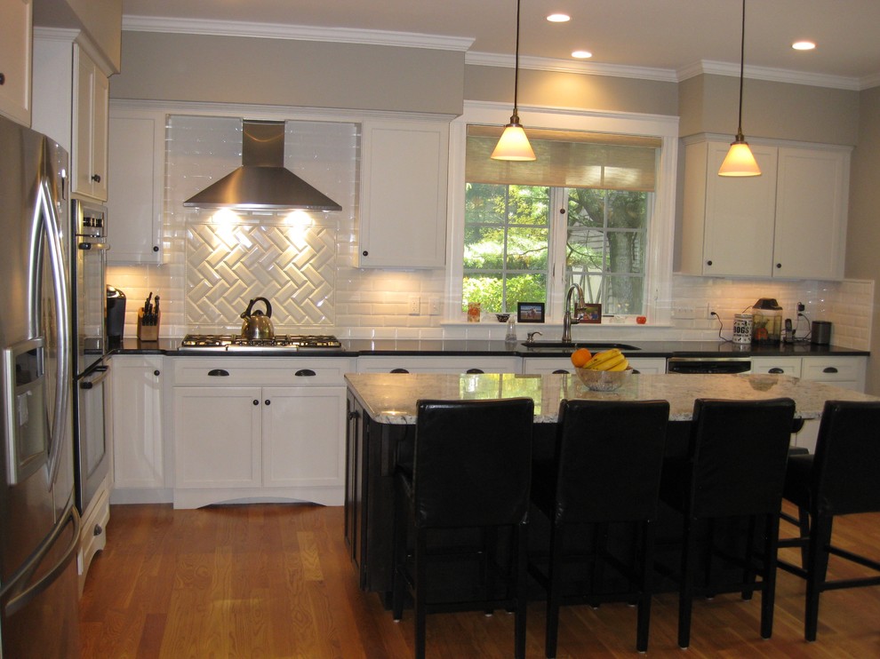 Transitional l-shaped medium tone wood floor eat-in kitchen photo in Boston with an undermount sink, shaker cabinets, white cabinets, granite countertops, white backsplash, ceramic backsplash, stainless steel appliances, an island and black countertops