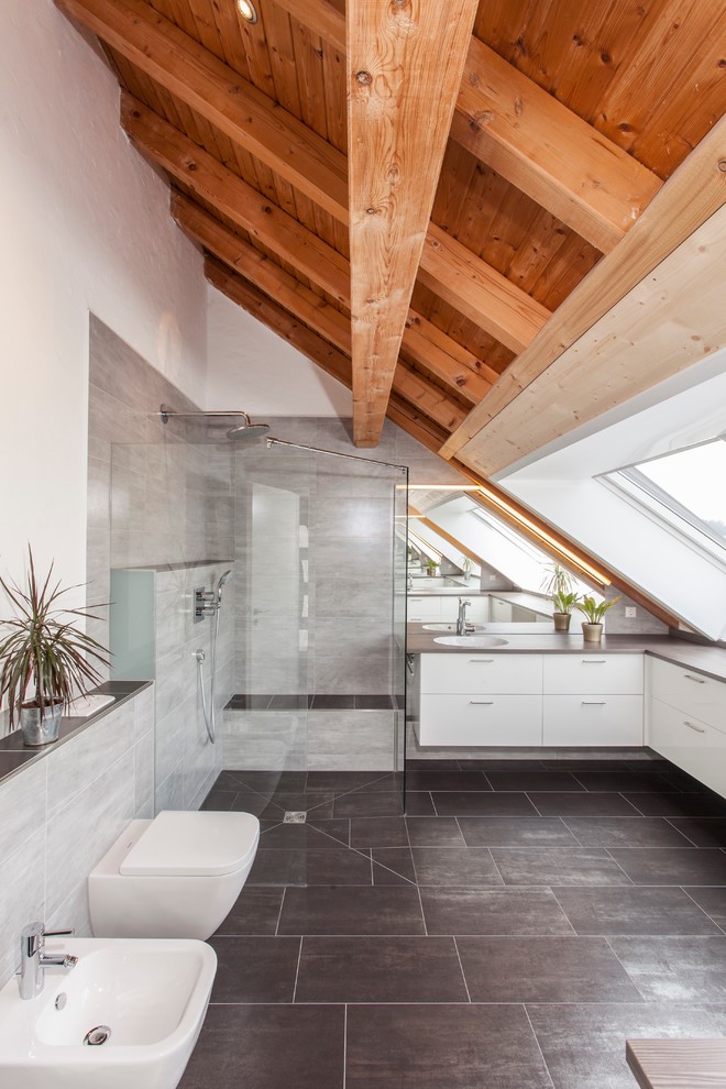 Large contemporary master bathroom in Munich with flat-panel cabinets, white cabinets, a wall-mount toilet, gray tile, white walls, slate floors and an open shower.