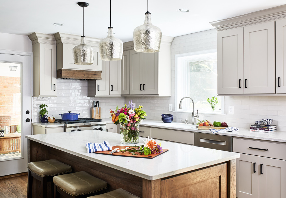 This is an example of a transitional l-shaped kitchen in DC Metro with shaker cabinets, grey cabinets, white splashback, subway tile splashback, stainless steel appliances, dark hardwood floors, with island, brown floor and white benchtop.