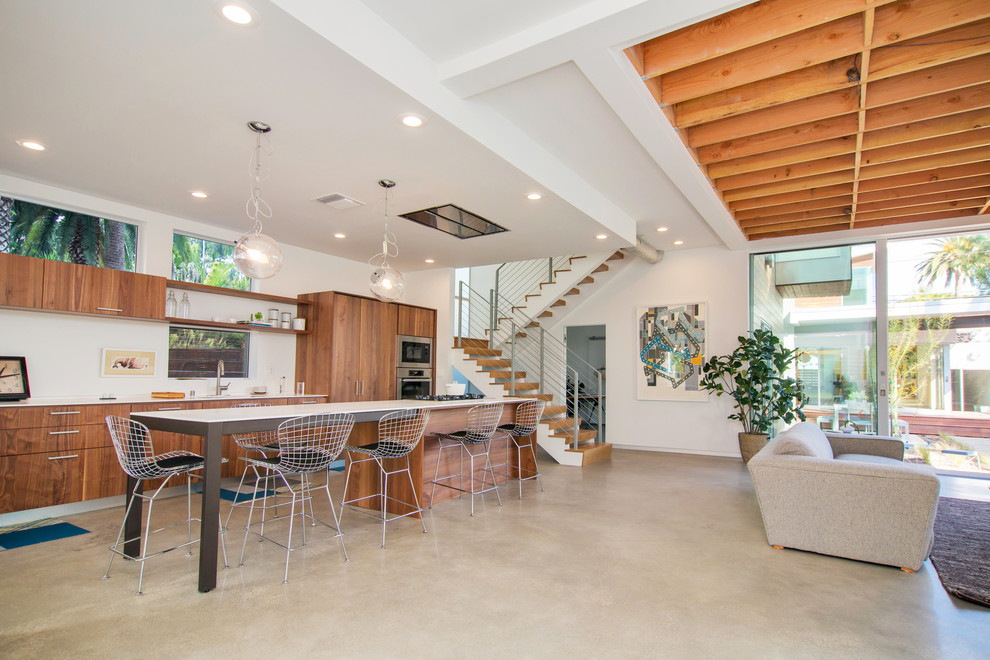 This is an example of a large contemporary galley open plan kitchen in Los Angeles with flat-panel cabinets, medium wood cabinets, stainless steel appliances, an undermount sink, solid surface benchtops, concrete floors and with island.