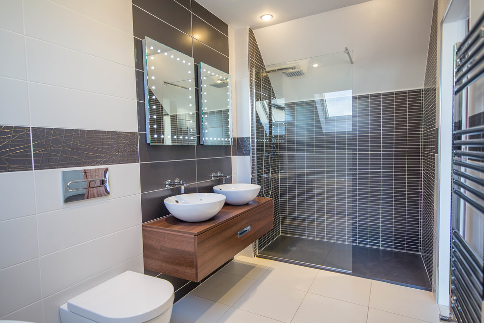 Photo of a mid-sized contemporary bathroom in Cork with an open shower, a one-piece toilet, multi-coloured tile, ceramic floors, white floor, a sliding shower screen, flat-panel cabinets, medium wood cabinets, multi-coloured walls, wood benchtops and brown benchtops.