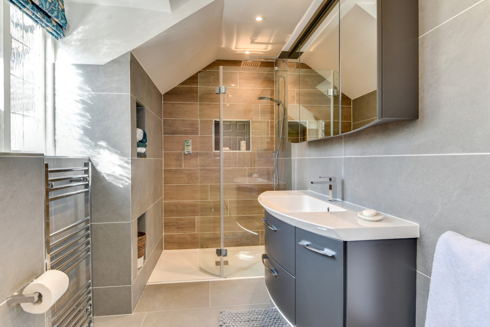Inspiration for a large modern grey and white ensuite bathroom in Sussex with flat-panel cabinets, grey cabinets, a freestanding bath, a walk-in shower, a one-piece toilet, grey tiles, ceramic tiles, grey walls, ceramic flooring, a built-in sink, glass worktops, grey floors, an open shower, white worktops, feature lighting, a single sink and a floating vanity unit.