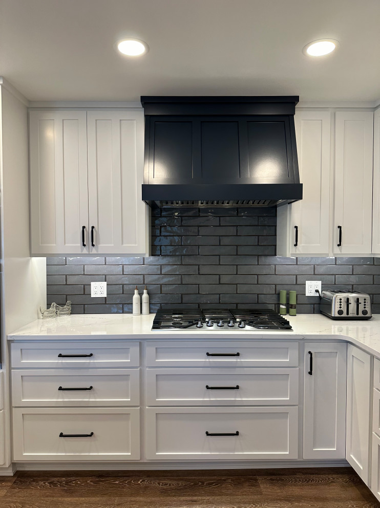 Inspiration for a mid-sized transitional l-shaped medium tone wood floor and brown floor open concept kitchen remodel with an undermount sink, recessed-panel cabinets, white cabinets, quartz countertops, gray backsplash, ceramic backsplash, stainless steel appliances, an island and white countertops