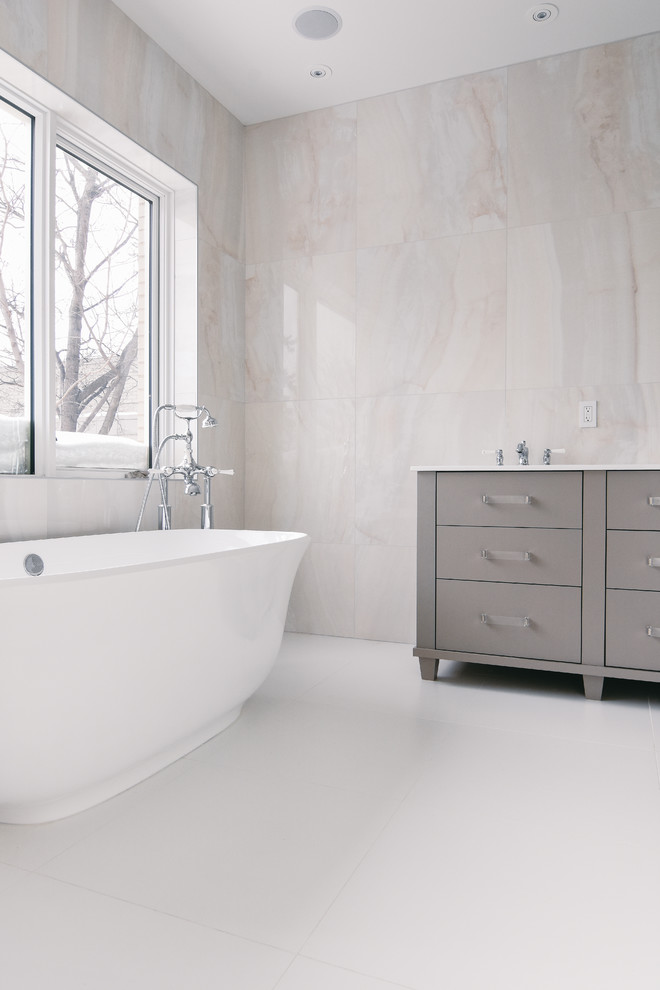 Inspiration for a large contemporary master bathroom in Montreal with flat-panel cabinets, grey cabinets, a freestanding tub, white tile, porcelain tile, porcelain floors, an undermount sink and engineered quartz benchtops.
