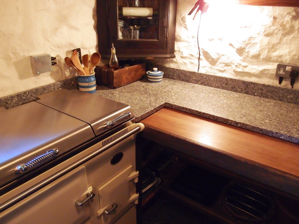 This is an example of a small rustic u-shaped enclosed kitchen in Cornwall with a belfast sink, shaker cabinets, dark wood cabinets, granite worktops, white appliances, slate flooring, no island, grey floors, grey worktops and exposed beams.