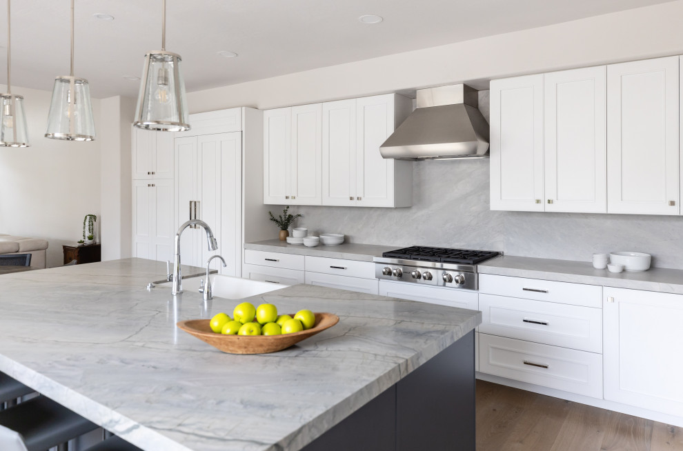 Large transitional medium tone wood floor and brown floor eat-in kitchen photo in Phoenix with a farmhouse sink, recessed-panel cabinets, white cabinets, quartzite countertops, beige backsplash, stone slab backsplash, paneled appliances, an island and gray countertops