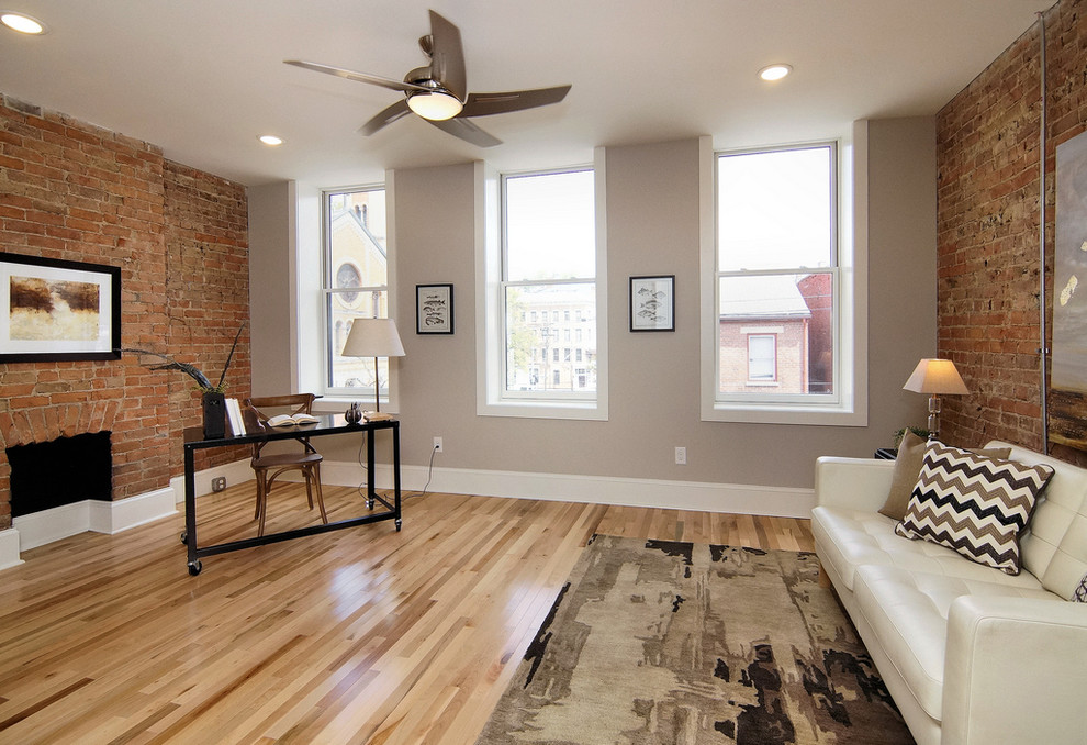 Large industrial study room in Cincinnati with grey walls, light hardwood floors, a freestanding desk, a standard fireplace, a brick fireplace surround and beige floor.