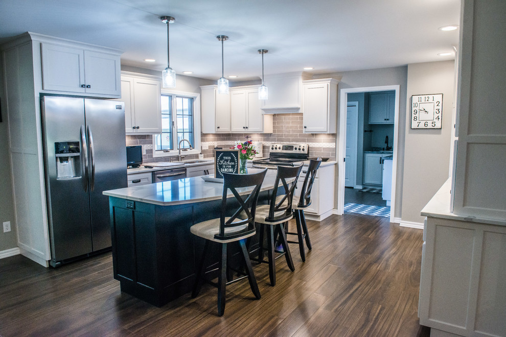 Large transitional u-shaped laminate floor and brown floor eat-in kitchen photo with a double-bowl sink, shaker cabinets, white cabinets, quartz countertops, gray backsplash, subway tile backsplash, stainless steel appliances, an island and white countertops