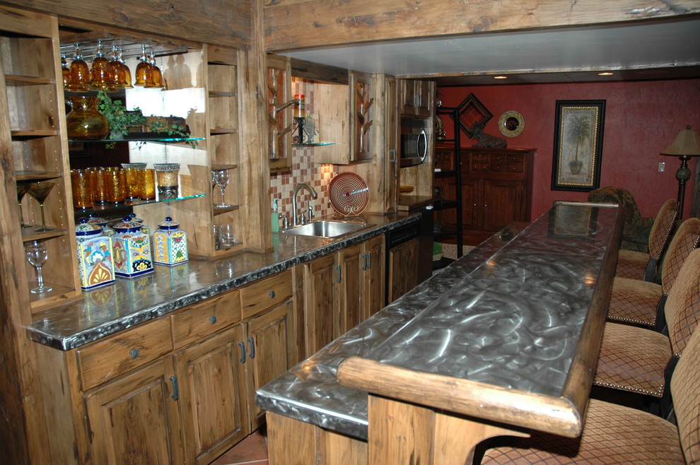 This is an example of a large country galley seated home bar in Wichita with raised-panel cabinets, light wood cabinets, zinc benchtops, multi-coloured splashback, mosaic tile splashback, terra-cotta floors, red floor and grey benchtop.