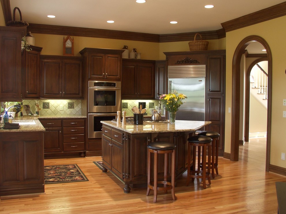 Inspiration for a large u-shaped medium tone wood floor eat-in kitchen remodel with an undermount sink, raised-panel cabinets, white cabinets, granite countertops, beige backsplash, subway tile backsplash, stainless steel appliances and a peninsula