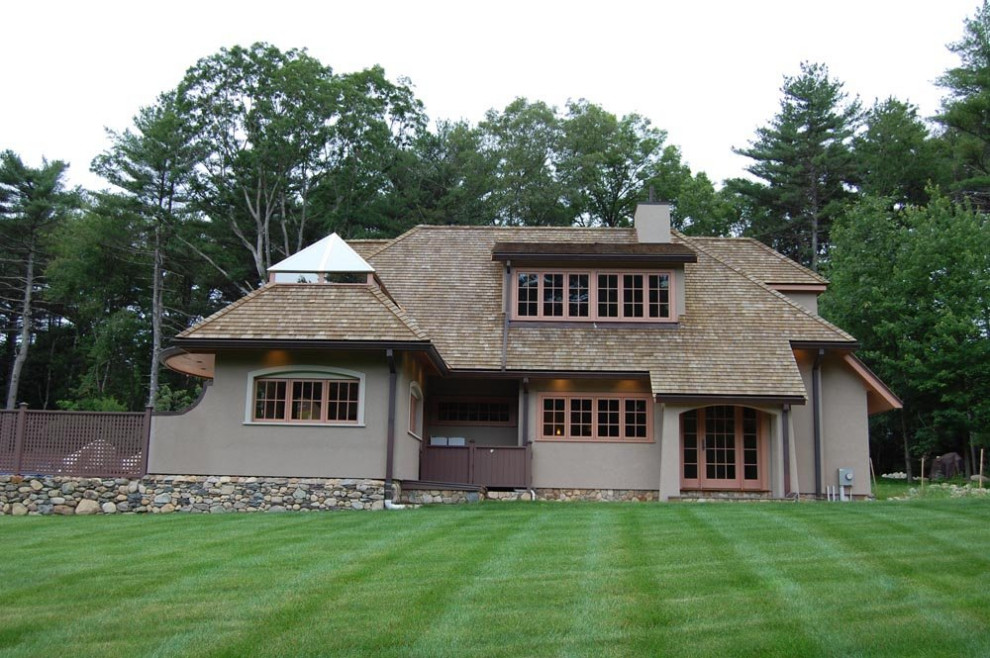 Example of a large arts and crafts beige two-story stucco house exterior design in Boston with a brown roof