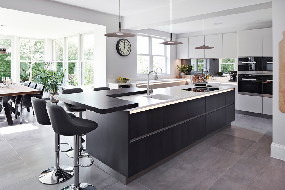Photo of an expansive contemporary u-shaped eat-in kitchen in Surrey with an integrated sink, flat-panel cabinets, mirror splashback, black appliances, porcelain floors, with island, grey floor and white benchtop.