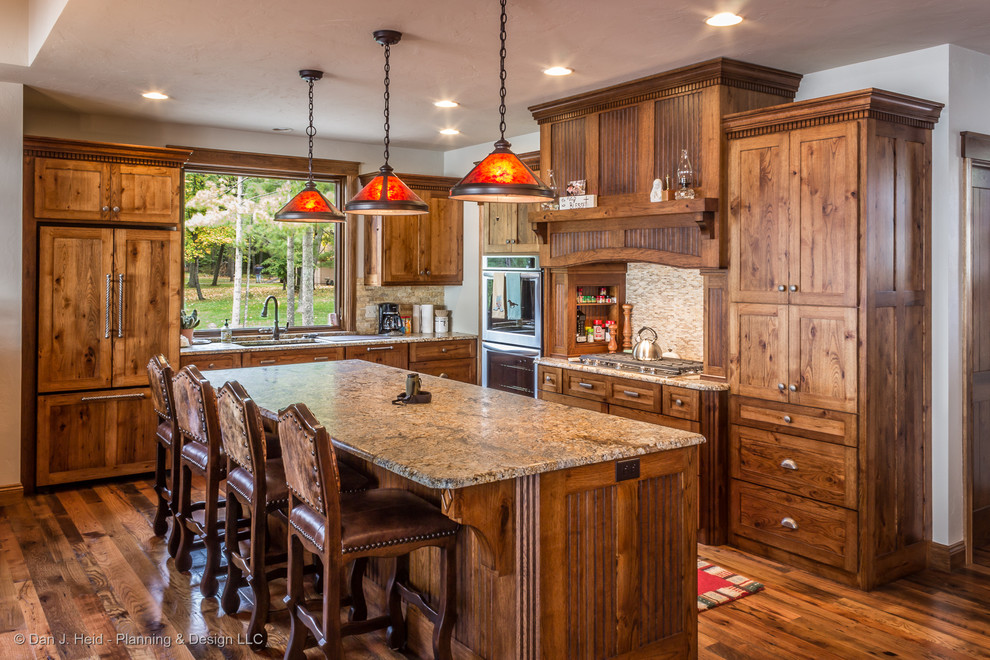 This is an example of a mid-sized country l-shaped eat-in kitchen in Minneapolis with an undermount sink, flat-panel cabinets, medium wood cabinets, granite benchtops, brown splashback, ceramic splashback, stainless steel appliances, medium hardwood floors, with island and brown floor.