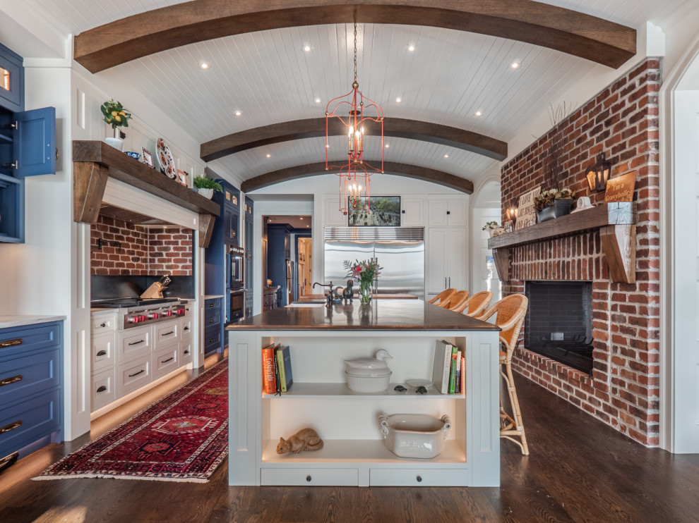 Design ideas for a traditional l-shaped kitchen in Other with a farmhouse sink, shaker cabinets, white cabinets, red splashback, brick splashback, stainless steel appliances, dark hardwood floors, with island, brown floor, white benchtop, exposed beam and vaulted.