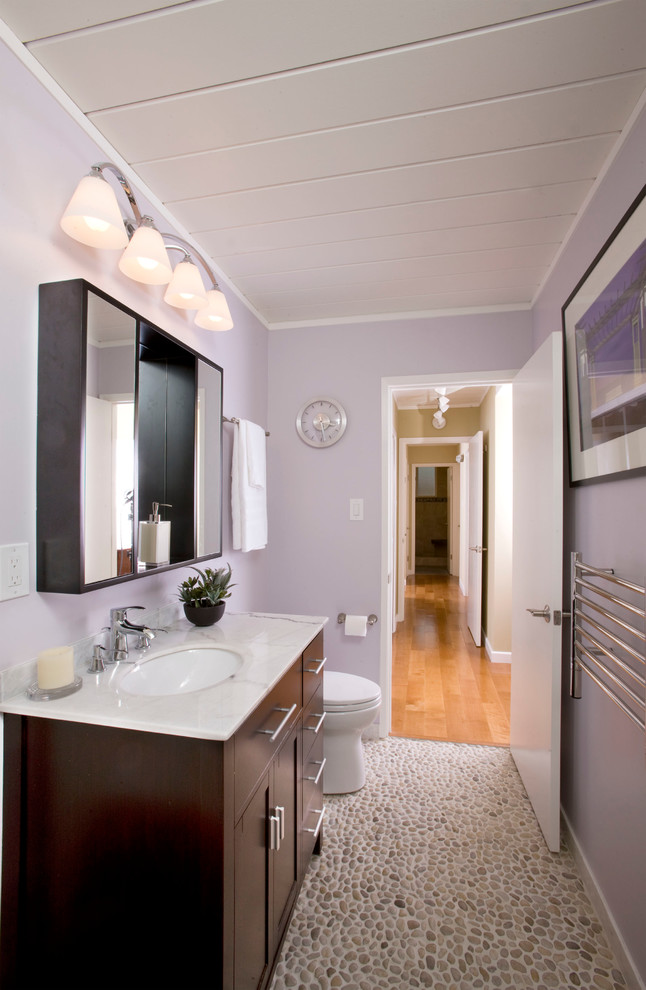 This is an example of a small transitional kids bathroom in San Francisco with shaker cabinets, black cabinets, an alcove tub, a shower/bathtub combo, a one-piece toilet, white tile, porcelain tile, pebble tile floors, an undermount sink, marble benchtops, grey floor, a shower curtain, white benchtops, a single vanity, a freestanding vanity, timber and purple walls.