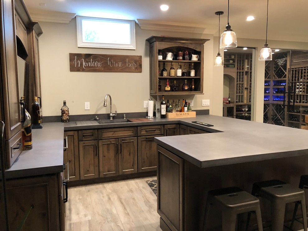 Inspiration for a mid-sized country u-shaped seated home bar in New York with an undermount sink, recessed-panel cabinets, dark wood cabinets, solid surface benchtops, light hardwood floors, beige floor and grey benchtop.