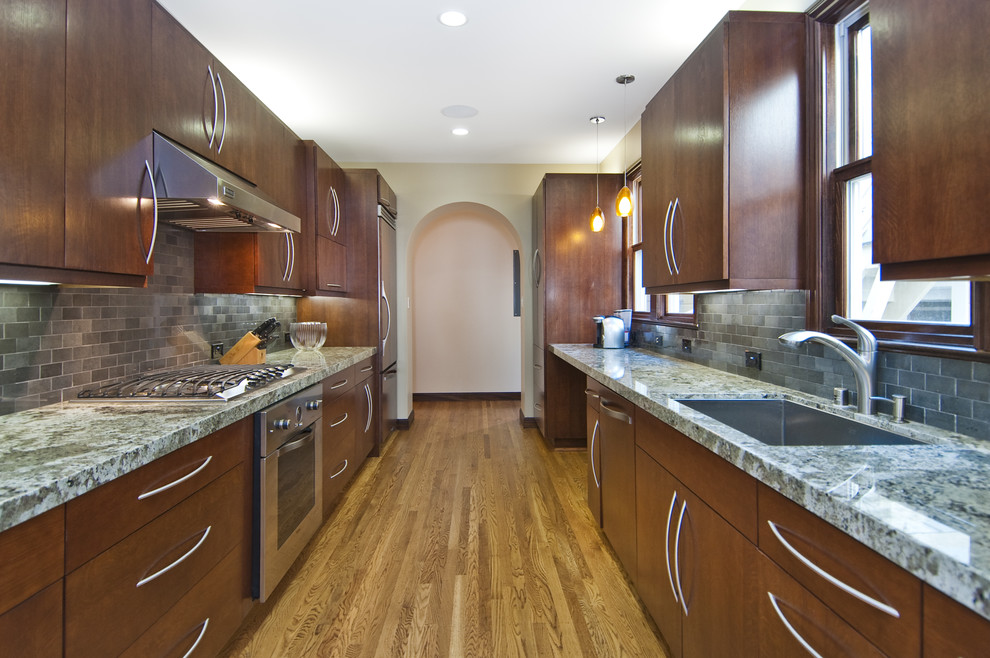 This is an example of a transitional galley separate kitchen in San Francisco with stainless steel appliances, an undermount sink, flat-panel cabinets, dark wood cabinets, grey splashback and subway tile splashback.
