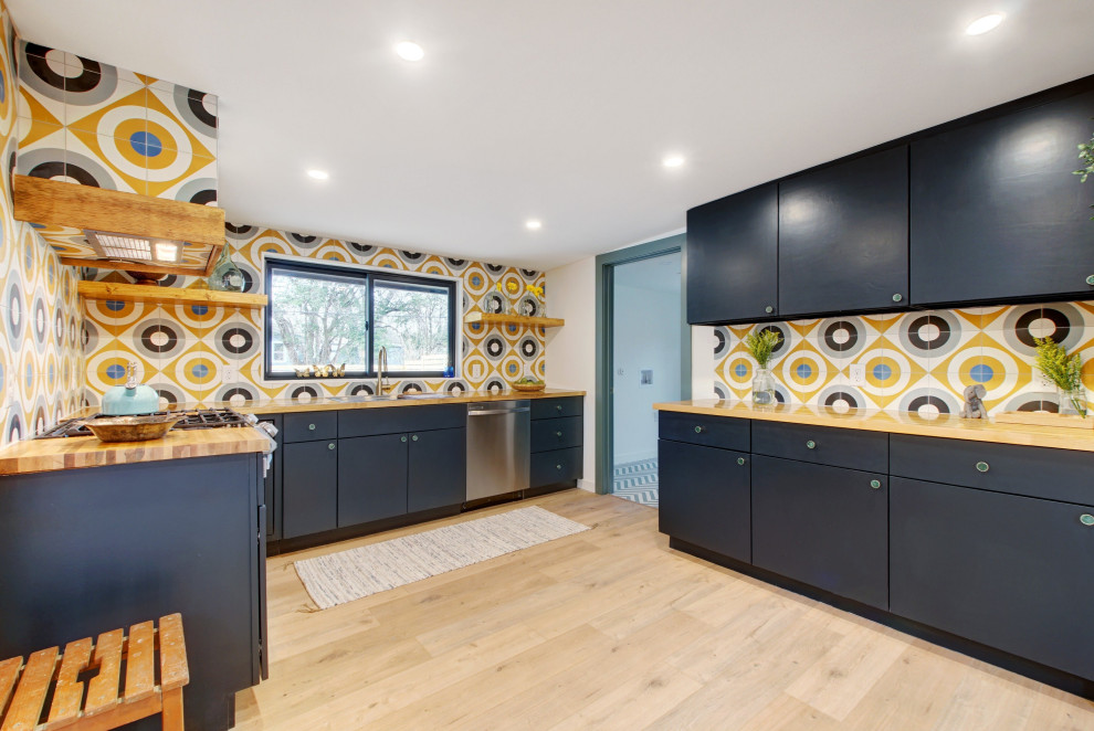 This is an example of a large midcentury u-shaped eat-in kitchen in Austin with a single-bowl sink, flat-panel cabinets, black cabinets, wood benchtops, multi-coloured splashback, cement tile splashback, stainless steel appliances, laminate floors, no island, beige floor and brown benchtop.