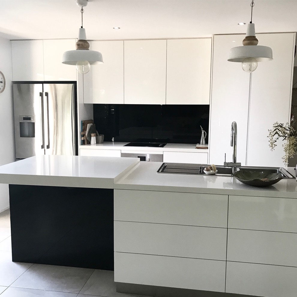 Photo of a mid-sized contemporary single-wall eat-in kitchen in Other with a drop-in sink, flat-panel cabinets, white cabinets, limestone benchtops, black splashback, ceramic splashback, stainless steel appliances, cement tiles, with island and grey floor.