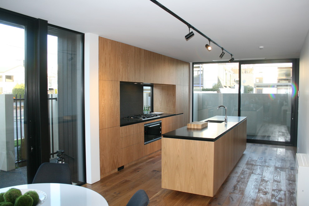 Mid-sized modern galley eat-in kitchen in Christchurch with an undermount sink, flat-panel cabinets, light wood cabinets, quartz benchtops, black splashback, mosaic tile splashback, stainless steel appliances, medium hardwood floors, with island and brown floor.