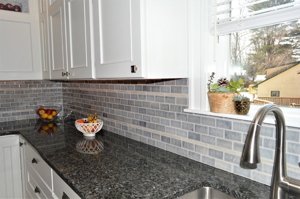 Mid-sized transitional l-shaped medium tone wood floor eat-in kitchen photo with an undermount sink, recessed-panel cabinets, white cabinets, granite countertops, gray backsplash, cement tile backsplash, stainless steel appliances, a peninsula and blue countertops