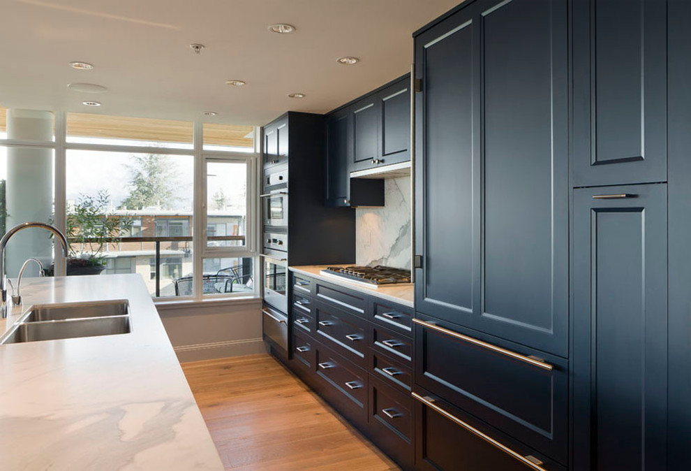 Mid-sized transitional l-shaped open plan kitchen in Vancouver with an undermount sink, recessed-panel cabinets, blue cabinets, marble benchtops, white splashback, marble splashback, stainless steel appliances, medium hardwood floors, with island and brown floor.