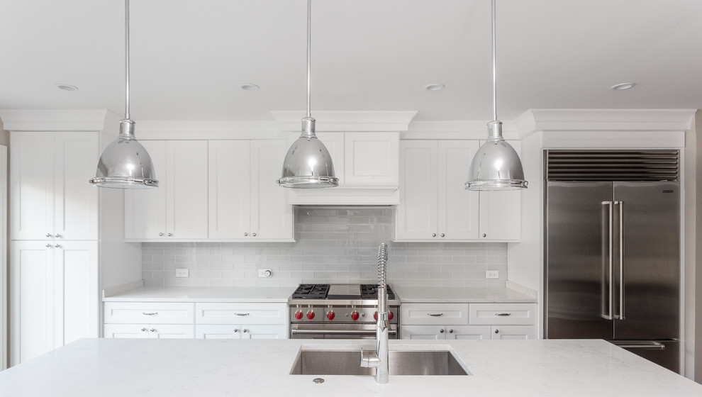 Kitchen - large transitional galley dark wood floor kitchen idea in Chicago with an undermount sink, shaker cabinets, white cabinets, quartzite countertops, white backsplash, glass tile backsplash, stainless steel appliances and an island