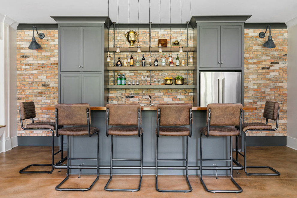 Design ideas for a mid-sized transitional galley seated home bar in Atlanta with an undermount sink, shaker cabinets, grey cabinets, wood benchtops, red splashback, brick splashback, concrete floors, red floor and brown benchtop.