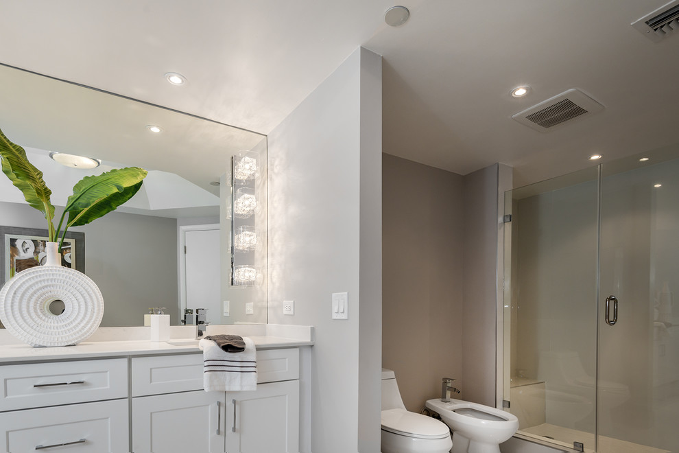 This is an example of a mid-sized contemporary master bathroom in Miami with shaker cabinets, white cabinets, a freestanding tub, a shower/bathtub combo, a one-piece toilet, white tile, porcelain tile, grey walls, porcelain floors, an undermount sink and engineered quartz benchtops.
