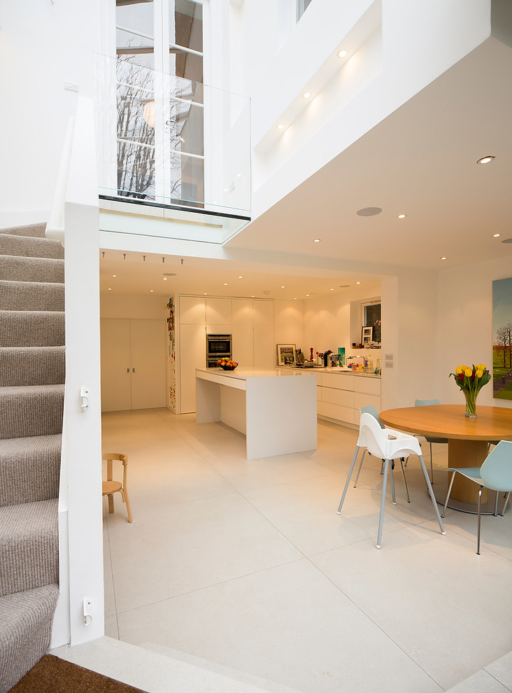 Large contemporary l-shaped eat-in kitchen in London with flat-panel cabinets, white cabinets, stainless steel appliances, with island and beige floor.