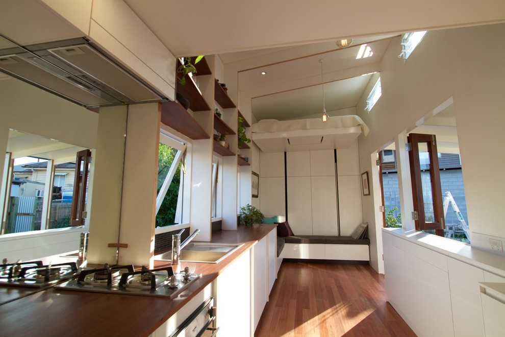 Photo of a small modern galley eat-in kitchen in Brisbane with white cabinets, wood benchtops, black splashback, mirror splashback, medium hardwood floors and no island.