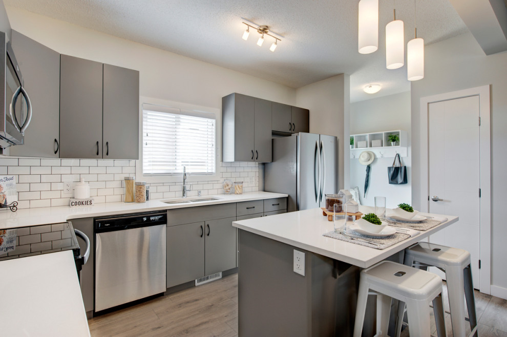 Design ideas for a small transitional l-shaped eat-in kitchen in Calgary with an undermount sink, flat-panel cabinets, grey cabinets, quartzite benchtops, white splashback, ceramic splashback, stainless steel appliances, laminate floors, with island, grey floor and white benchtop.