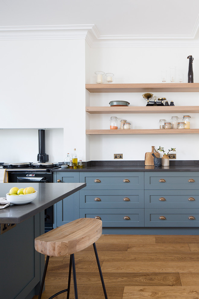 This is an example of a mid-sized eclectic single-wall eat-in kitchen in Edinburgh with a farmhouse sink, shaker cabinets, blue cabinets, quartz benchtops, black appliances and with island.