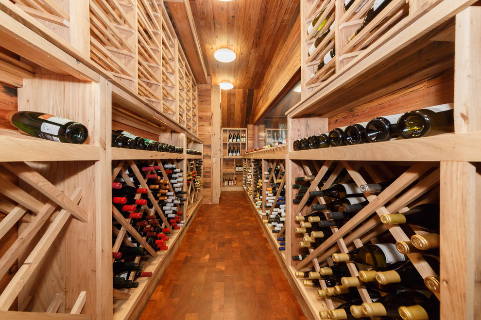 Large country wine cellar in New York with dark hardwood floors and diamond bins.