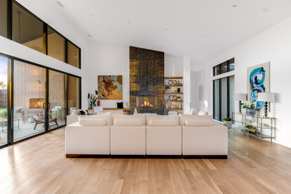 Inspiration for a large midcentury open concept living room in Dallas with white walls, light hardwood floors, a standard fireplace, a tile fireplace surround, brown floor and vaulted.