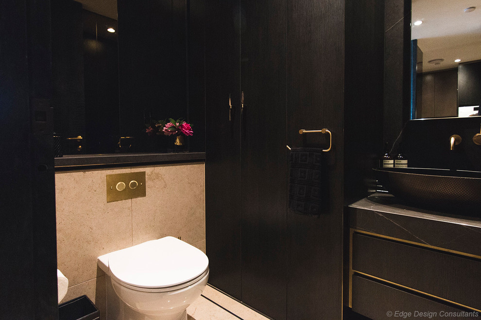 This is an example of a mid-sized modern powder room in Sydney with flat-panel cabinets, dark wood cabinets, a wall-mount toilet, gray tile, porcelain tile, grey walls, porcelain floors, a vessel sink, tile benchtops, beige floor and grey benchtops.