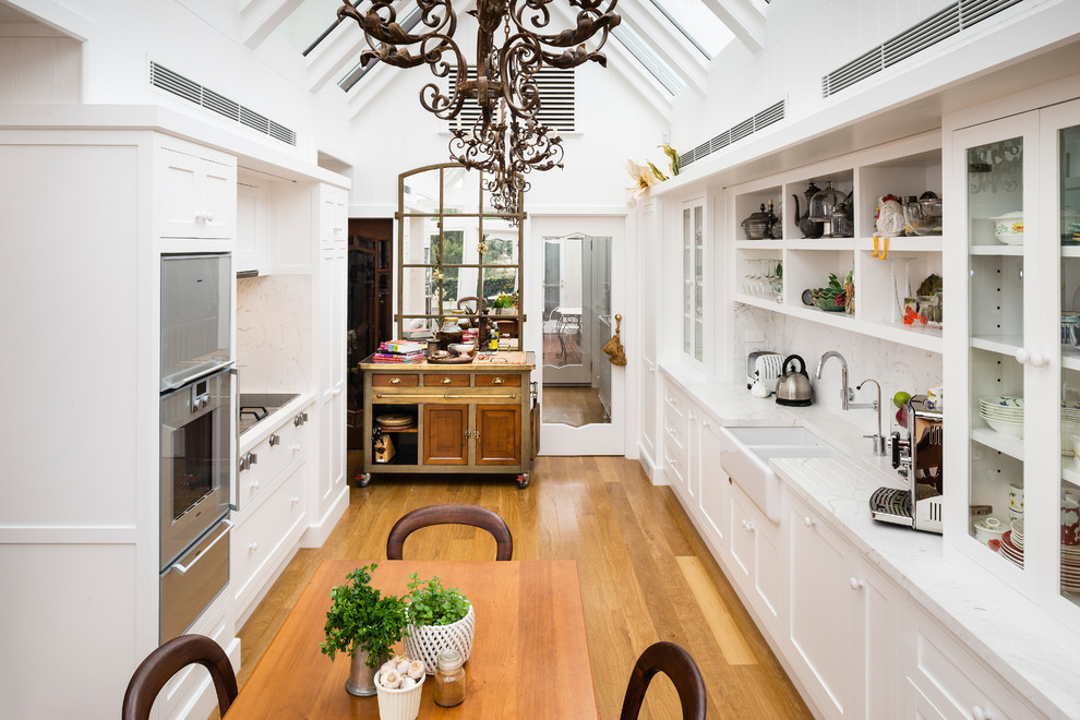 Design ideas for a traditional galley eat-in kitchen in Melbourne with a farmhouse sink, recessed-panel cabinets, white cabinets and stainless steel appliances.