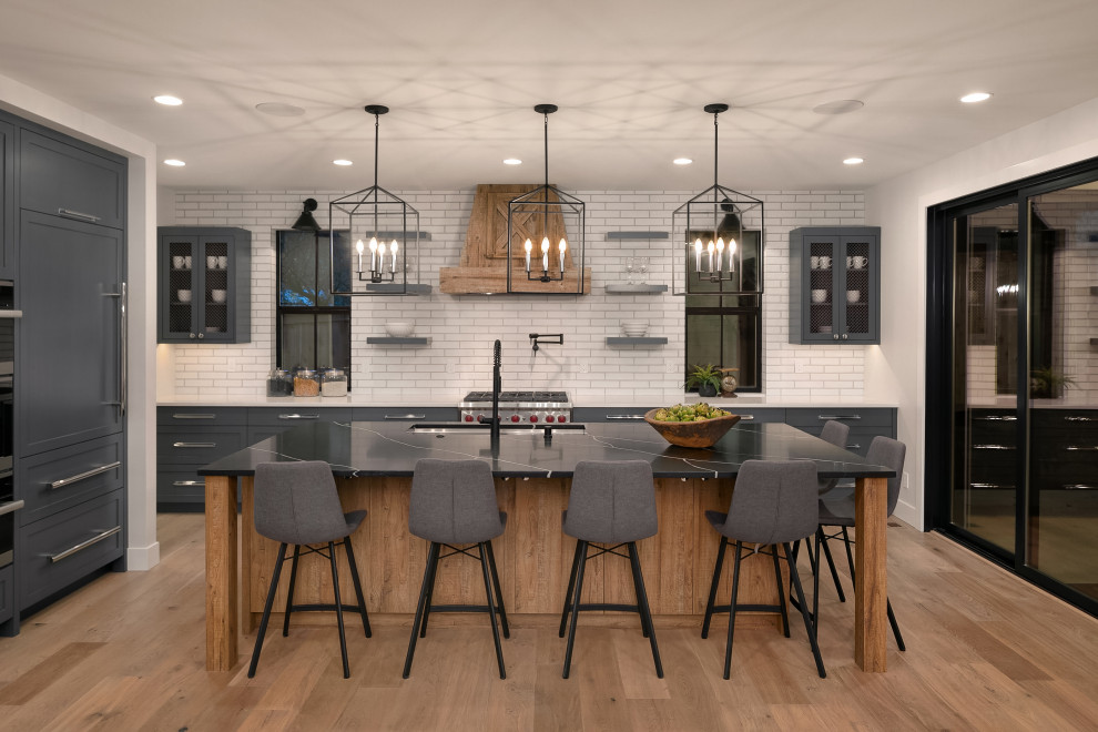 Expansive country l-shaped kitchen in Seattle with an undermount sink, shaker cabinets, grey cabinets, white splashback, subway tile splashback, panelled appliances, medium hardwood floors, with island, beige floor and black benchtop.