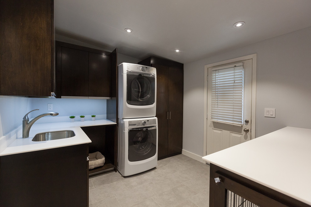 Inspiration for a mid-sized contemporary u-shaped laundry room in Dallas with an undermount sink, flat-panel cabinets, dark wood cabinets, stainless steel benchtops, white splashback, glass sheet splashback and ceramic floors.