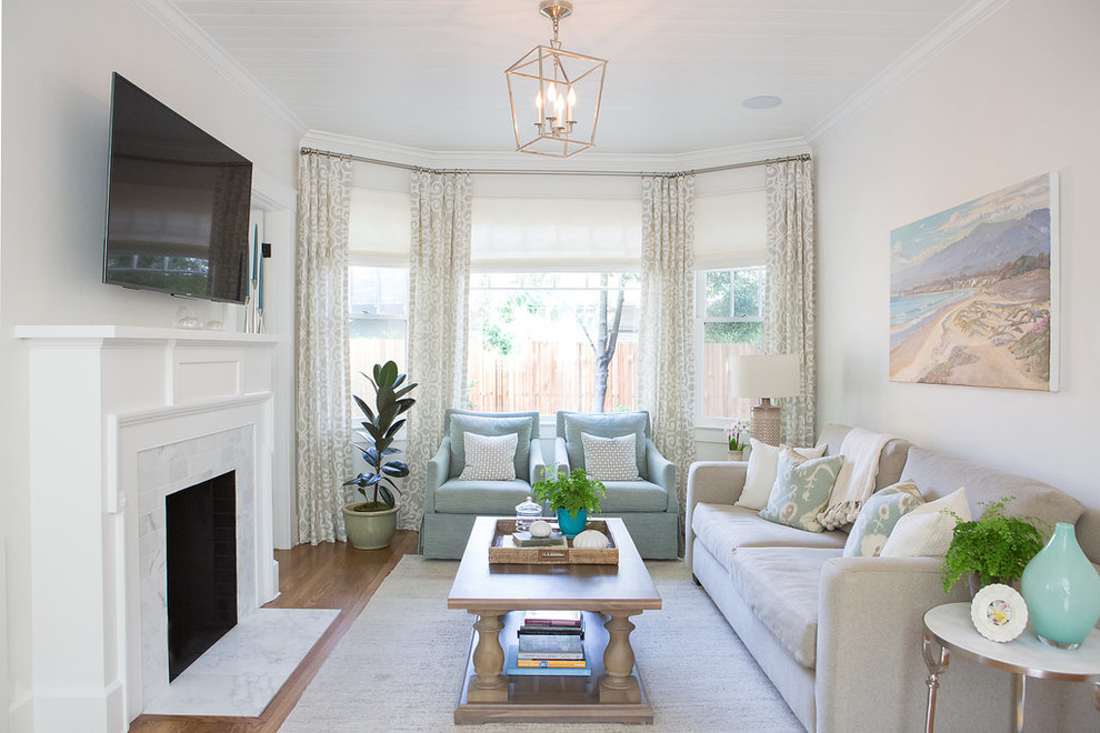 Inspiration for a mid-sized beach style open concept family room in Santa Barbara with white walls, medium hardwood floors, a standard fireplace, a plaster fireplace surround, a wall-mounted tv and brown floor.