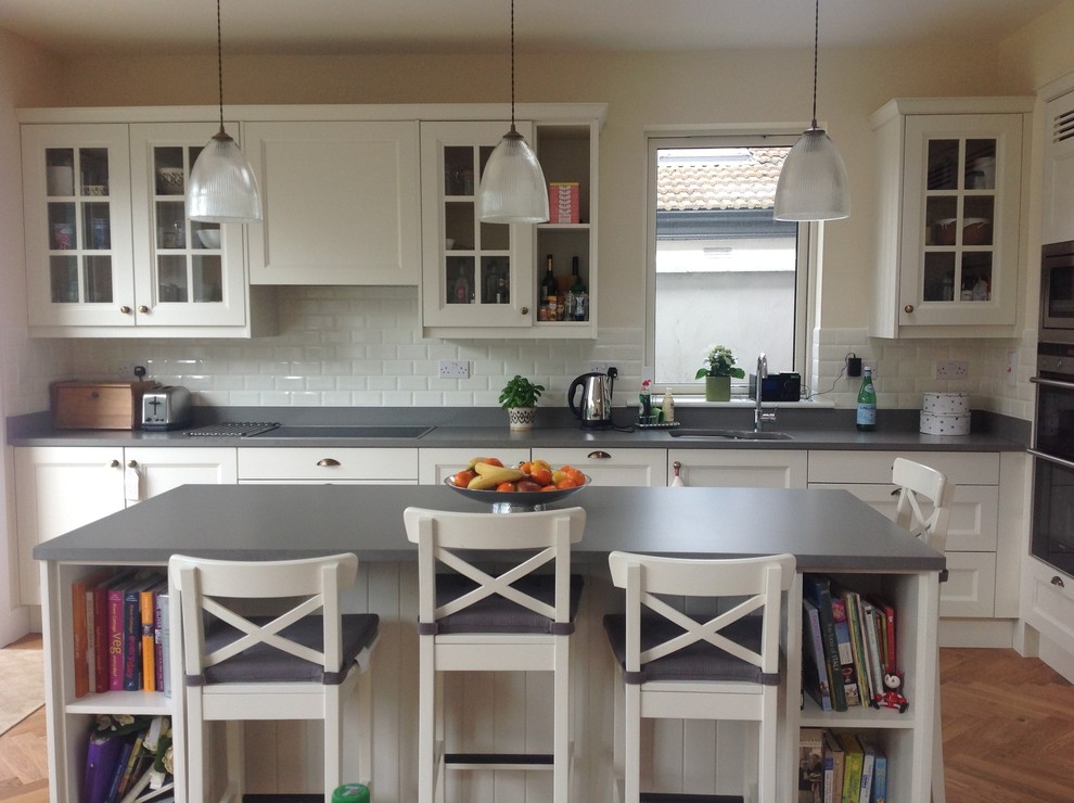 Photo of a mid-sized l-shaped eat-in kitchen in Dublin with an undermount sink, flat-panel cabinets, light wood cabinets, recycled glass benchtops, white splashback, ceramic splashback, stainless steel appliances, medium hardwood floors and with island.