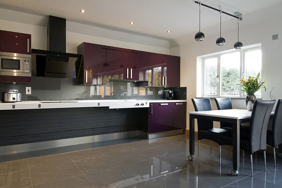 This is an example of a mid-sized contemporary l-shaped open plan kitchen in Essex with an integrated sink, flat-panel cabinets, purple cabinets, concrete benchtops, metallic splashback, glass sheet splashback, stainless steel appliances, porcelain floors and grey floor.