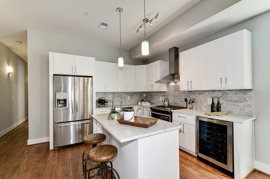 Example of a small transitional l-shaped medium tone wood floor eat-in kitchen design in DC Metro with an undermount sink, shaker cabinets, white cabinets, marble countertops, gray backsplash, subway tile backsplash, stainless steel appliances and an island