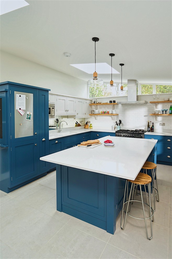 This is an example of a transitional u-shaped eat-in kitchen in Hertfordshire with shaker cabinets, blue cabinets, quartzite benchtops, metallic splashback, mirror splashback, stainless steel appliances and with island.