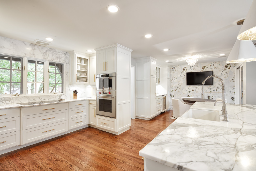 Eat-in kitchen - large transitional u-shaped medium tone wood floor and brown floor eat-in kitchen idea with a farmhouse sink, shaker cabinets, white cabinets, marble countertops, white backsplash, marble backsplash, stainless steel appliances and an island