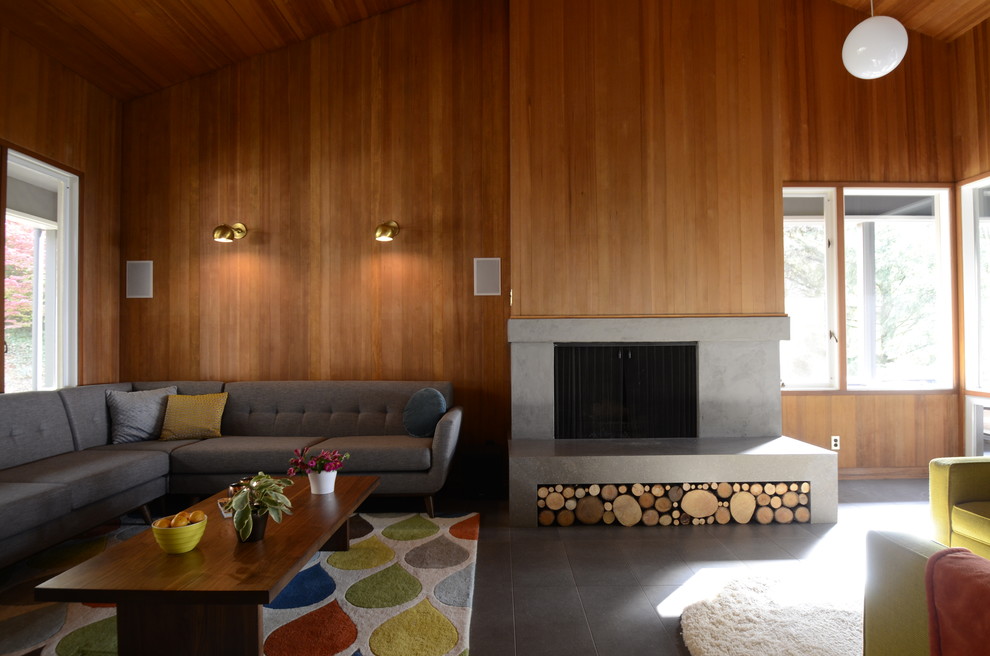 Photo of a large midcentury open concept family room in Portland with a standard fireplace, a stone fireplace surround, brown walls, porcelain floors, a wall-mounted tv and grey floor.