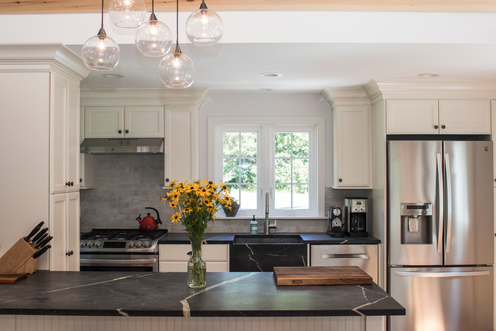 Mid-sized transitional galley open concept kitchen photo in Boston with a farmhouse sink, recessed-panel cabinets, white cabinets, soapstone countertops, gray backsplash, stainless steel appliances and a peninsula