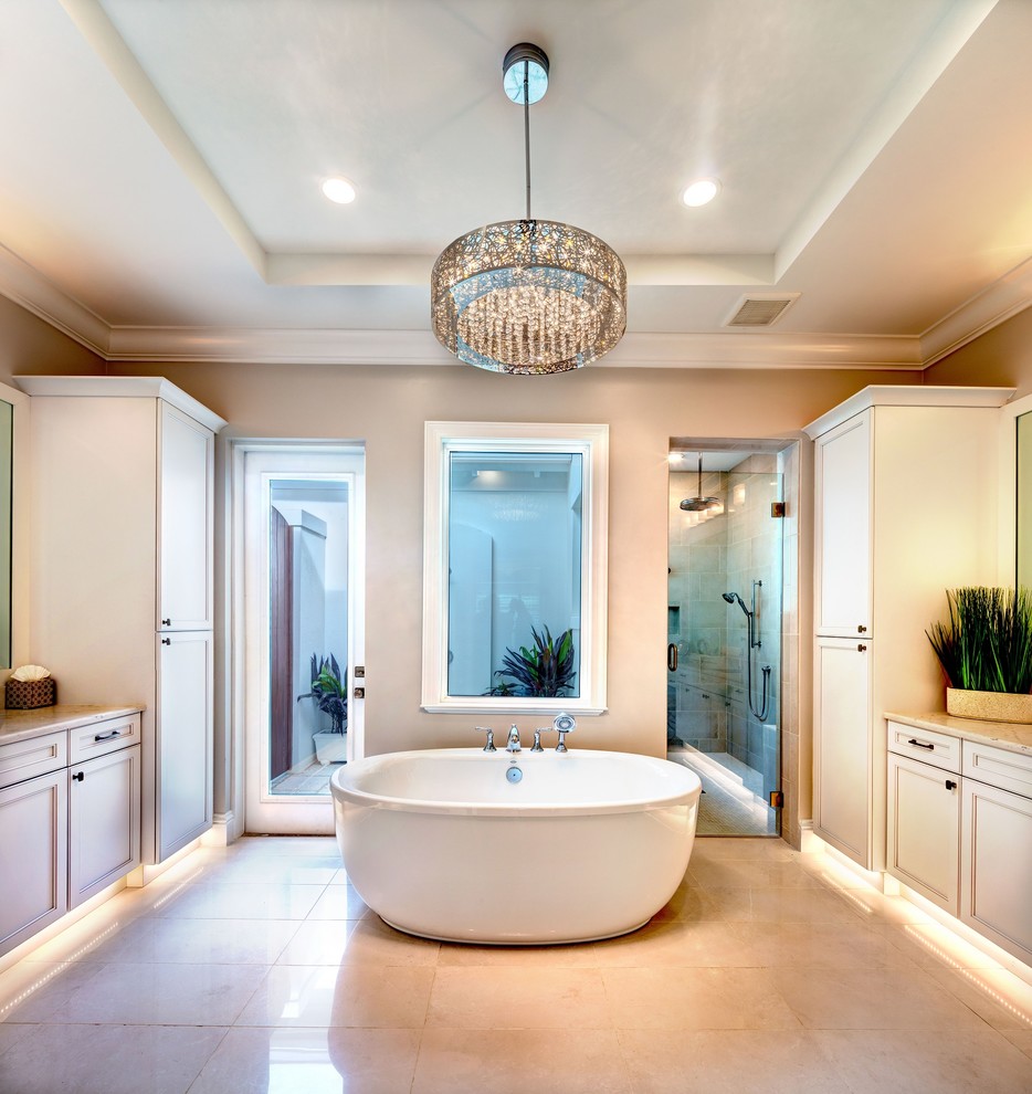 This is an example of a beach style master bathroom in Tampa with shaker cabinets, white cabinets, a freestanding tub, an alcove shower, white tile, porcelain tile, beige walls, porcelain floors, an undermount sink, engineered quartz benchtops, white floor and a hinged shower door.