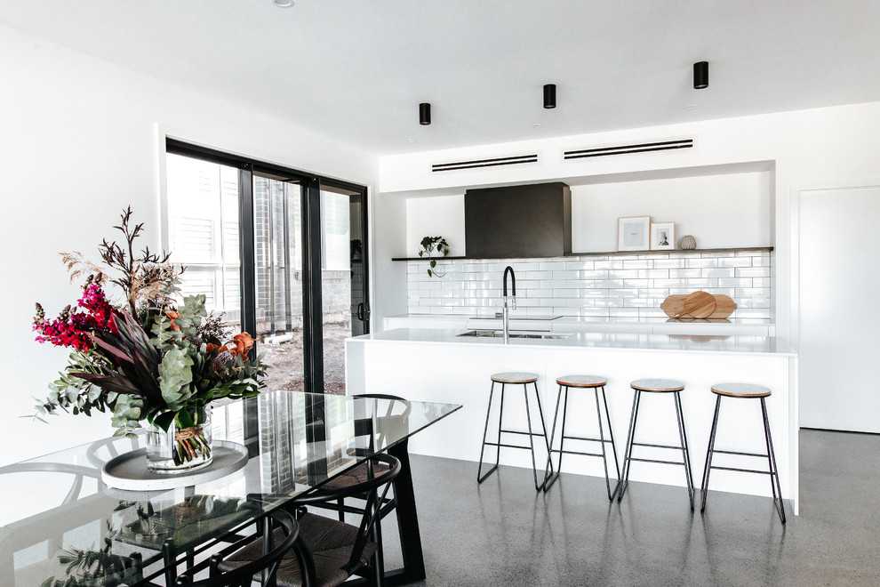 Mid-sized modern galley kitchen in Wollongong with a double-bowl sink, flat-panel cabinets, white cabinets, quartz benchtops, white splashback, ceramic splashback, stainless steel appliances, concrete floors, with island, grey floor and white benchtop.